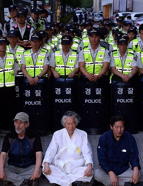 지난 10일 오후 서울 종로구 세종로 동십자각 인근에서 백기완 통일문제연구소장을 비롯한 '6.10 만민공동회' 참가자들이 경찰병력 앞에 앉아있다. 당초 '6.10 만민공동회'는 국립현대미술관 서울관에서 열릴 예정이였으나 경찰은 허가되지 않은 집회라고 주장하며 주요 진입로에 병력을 배치해 집회장소 출입을 차단했다. 뉴시스