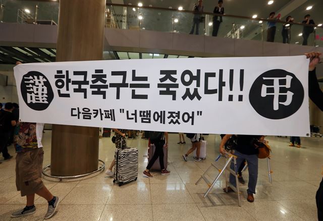 한국 축구 대표팀 선수들이 30일 오전 인천공항을 통해 귀국, 취재진과 인터뷰를 하고 있는 가운데 한쪽에서 일부 팬이 '한국 축구는 죽었다'라고 적힌 현수막을 들고 있다. 홍명보 감독이 이끄는 대표팀은 2014 브라질월드컵에서 H조 꼴찌로 조별리그에서 탈락했다. 연합뉴스