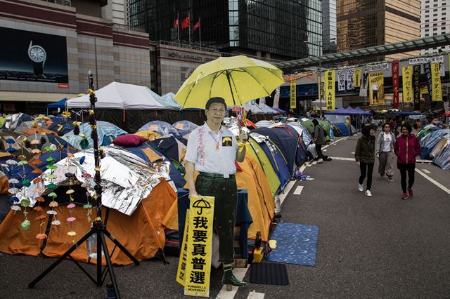 홍콩 도심 점거 시위가 48일째로 접어든 가운데 13일(현지시간) 시위대가 점령중인 애드미럴티지구 중앙정부청사 앞 시위대 텐트 앞에 노란 우산을 들고 있는 시진핑 중국 주석의 등신대가 세워져 있어 눈길을 끌고 있다. 한편 시위대가 15일 중국 당국자와의 면담을 위한 베이징방문을 강행하기로 했다. 홍콩=블룸버그 연합뉴스