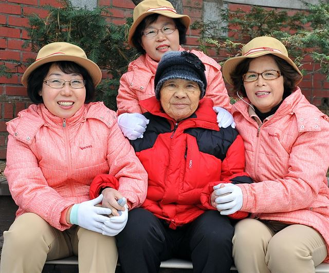 야쿠르트아줌마들이 '홀몸노인 돌봄사업'를 통해 방문하는 홀몸 할머니와 함께 손을 잡고 미소짓고 있다. 한국야쿠르트 제공