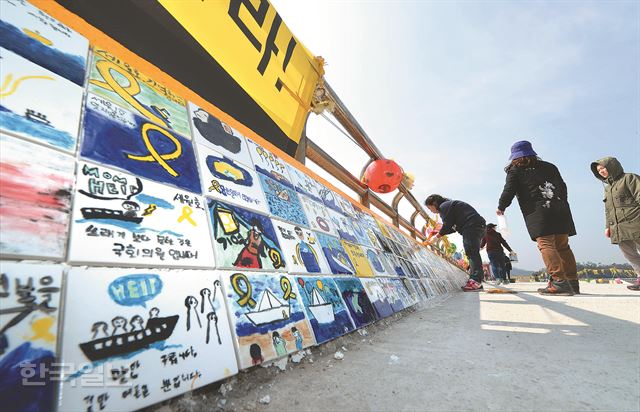 10일 오후 전남 진도군 팽목항에서 동화작가와 진도주민들이 세월호 참사에 대해 쓰고 그린 타일을 한 장씩 붙여 '기억의 벽'을 만들고 있다. 전국 수천명이 보내온 타일에는 '꼭 다시 태어나 줘' '엄마가 한 번 안아 주고 싶다' '진실을 규명하라'라는 글귀가 담겼다. 진도=신상순 선임기자 ssshin@hk.co.kr