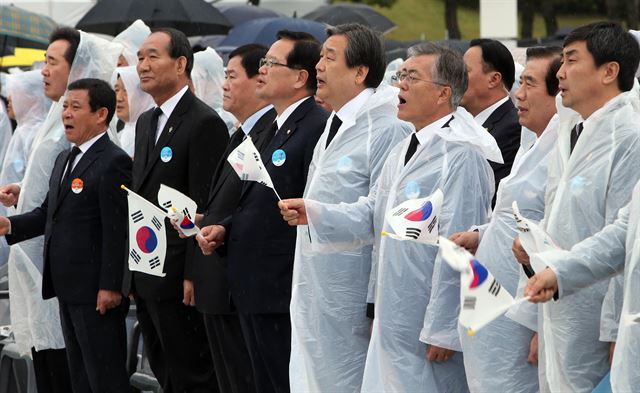 18일 광주 국립 5ㆍ18민주묘지에서 열린 5ㆍ18 광주민주화운동 기념식에서 대부분 참석자들이 임을 위한 행진곡을 따라 부르고 있다. 오른쪽부터 이종걸 새정치민주연합 원내대표, 한광옥 국민대통합위원장, 문재인 새정치연합 대표는 태극기를 흔들며 노래를 불렀고 김무성 새누리당 대표는 태극기 없이 노래만 따라 불렀지만, 태극기를 들고 노래를 따라 부르는 정의화 국회의장 옆에 나란히 선 최경환 경제부총리는 태극기만 든 채, 박승춘 보훈처장은 태극기도 들지 않은 채 입을 굳게 다물고 있다. 광주=연합뉴스