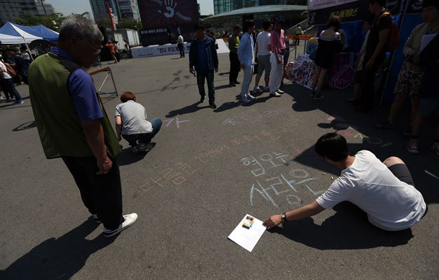 지난 16일 오후 서울역광장에서 열린 세계 성소수자 혐오 반대의 날 행사에서 동성애를 옹호하는 한 시민이 바닥에 메시지를 적자 길을 지나던 어르신이 이를 바라보고 있다. 연합뉴스