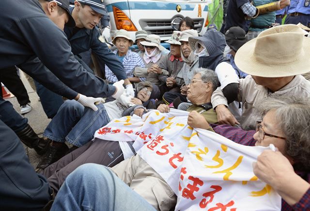 일본 정부가 오키나와현의 미군기지 이전에 대한반발에도 불구하고 공사를 강행하기로 결정한 가운데 29일(현지시간) 오키나와현 나고의 미군기지 캠프 슈왑 정문 앞에서 경찰들이 연좌 시위를 하던 시위자들에 대한 해산을 시도하고 있다. 나고=AP 연합뉴스