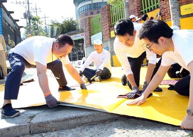 박용만(왼쪽) 두산 회장이 지난 9월14일 서울 중구 신당초등학교에서 임직원들과 함께 어린이들의 안전한 보행을 돕기 위한 옐로카펫을 설치하고 있다.