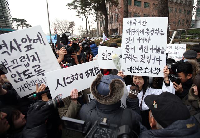 사회활동가이자 행위예술가인 홍승희씨가 6일 서울 종로구 주한일본대사관 앞에서 한일 위안부 합의에 대해 "더 이상 일본에 책임을 묻지 말라"고 주장하는 어버이연합 회원들에게 팻말을 들고 미소를 지어 보이고 있다. 연합뉴스