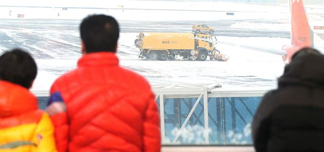 사상 초유의 제주공항 항공기 중단 사태가 3일째 이어진 25일 공항 체류객들이 다시 시작된 제설작업을 바라보고 있다. 제주=연합뉴스