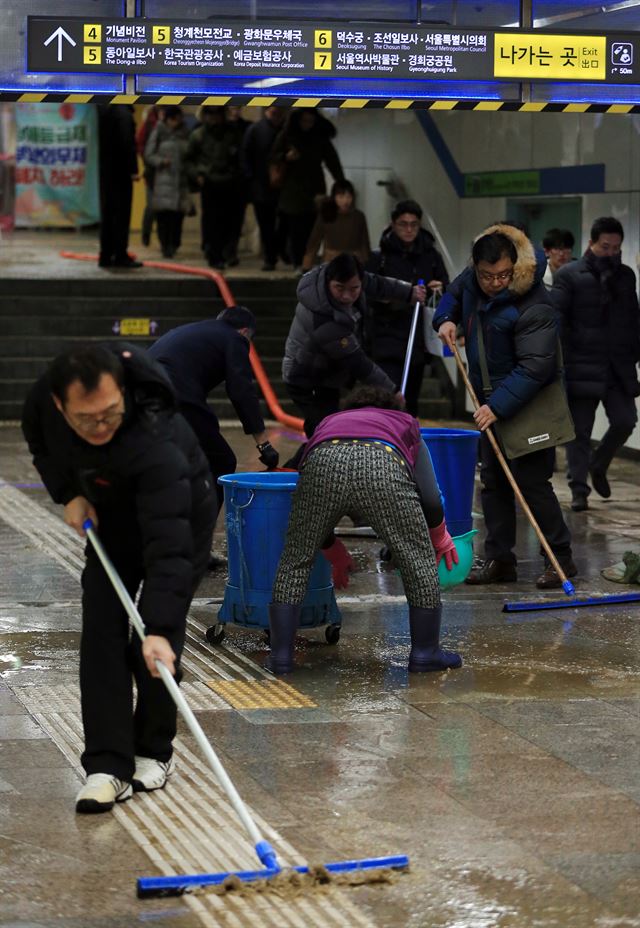 25일 오후 서울 지하철 5호선 광화문역 대합실에 물과 토사가 유입돼 역 관계자들이 쓰레받기 등으로 토사와 물을 플라스틱통에 담으며 복구 작업을 하고 있다. 연합뉴스