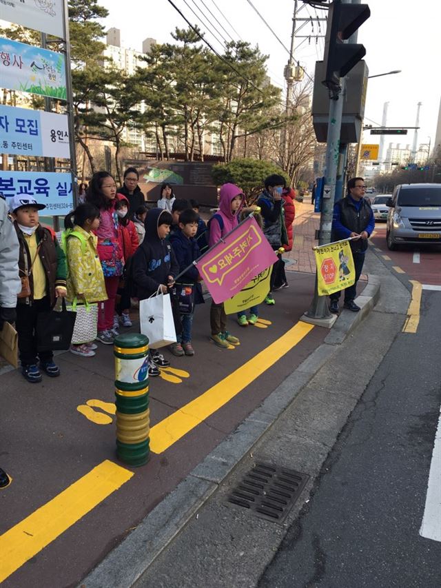 경기 용인 상현초등학교 학생들이 지난 17일 횡단보도 앞에 그려진 ‘노란 발자국’ 위에 서서 신호를 기다리고 있다. 이 발자국은 횡단보도 교통사고 예방을 위해 경기남부지방경찰청이 그려 넣었다. 경기남부청 제공