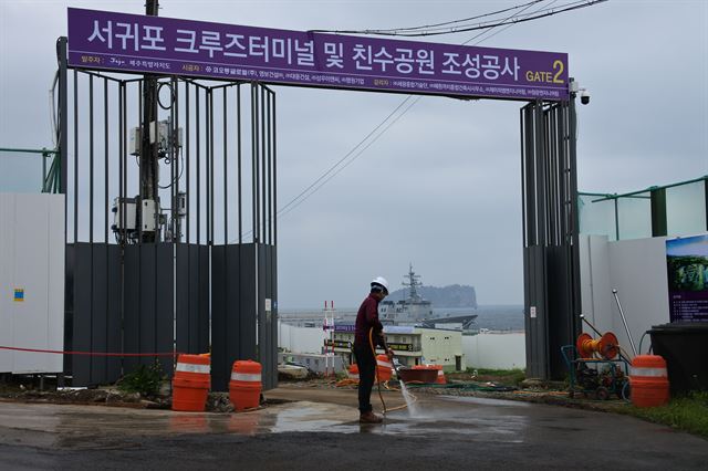 제주 서귀포시 제주민군복합항 크루즈터미널 공사현장 입구. 작업인부 뒤쪽으로 제주민군복합항에 정박 중인 해군 함정이 보인다. 제주=김영헌 기자.