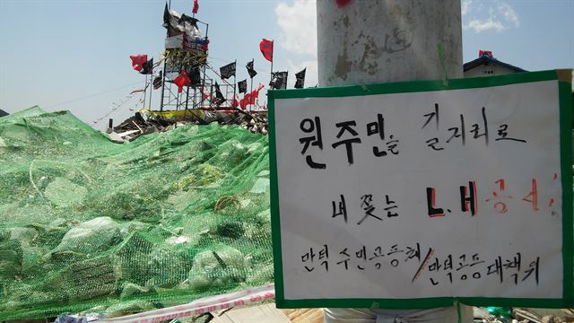 만덕5지구 전봇대에 부착된 항의 표지판 뒤로 최수영(50) 대표가 고공농성 중인 철탑이 보인다.