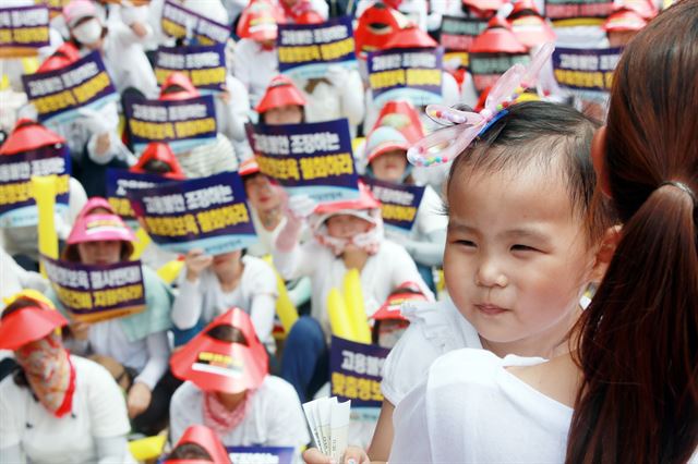 13일 서울 여의도 국회 인근에서 한국가정어린이집연합회 주최로 열린 맞춤형 보육 시행 반대 결의대회에서 한 어린이가 발언하는 부모의 품에 안겨 취재진을 바라보고 있다. 연합뉴스