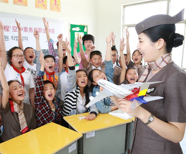 지난 6월 중국 장쑤성 옌청시 신탄소학교에서 아시아나항공 승무원이 모형비행기를 들고 학생들에게 승무원 업무에 대해 설명하고 있다. 아시아나항공은 이날 강연과 함께 학교에 컴퓨터 8대, 책걸상 400개, 책 1,000권 등을 기부했다. 아시아나항공 제공