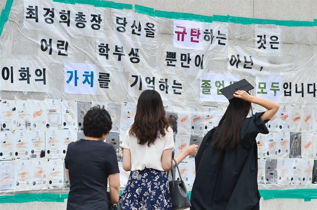 26일 오전 졸업식이 열린 서울 서대문구 이화여자대학교 정문에 학생 측이 최경희 총장 사퇴를 요구하며 내 건 졸업장 반납 게시물 앞으로 학생들과 가족들이 오가고 있다. 뉴스1