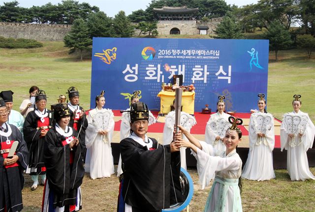 2016청주세계무예마스터십 조직위원장인 이시종 충북지사(가운데)가 1일 청주 상당산성 남문 앞에서 칠선녀로부터 성화를 전달받고 있고 있다. 이 성화는 청주시내 주요 거리를 돌아 2일 개회식에서 점화된다. 무예마스터십 조직위 제공