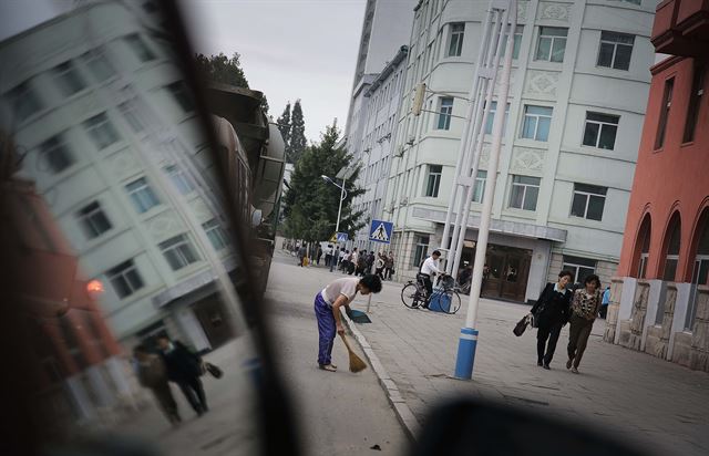 북한 평양에서 28일 아침 하루를 시작한 주민들이 각자의 행선지로 향하고 있는 가운데 한 여성이 도로부근을 청소하고 있다. 북한의 수도 평양은 여전히 세계 다른 나라 수도보다 매우 조용한 도시지만 매우 일찍 하루를 시작한다. AP 연합뉴스