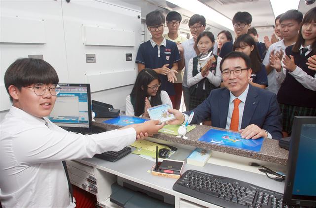 지난해 서울 관악구 소재 성보중학교에서 진행된 금융체험교육에서 신한은행 조용병(오른쪽) 은행장이 버스를 개조한 이동점포 뱅버드에서 은행원 직업체험 실습에 참가한 학생으로부터 통장을 받고 있다. 신한은행 제공