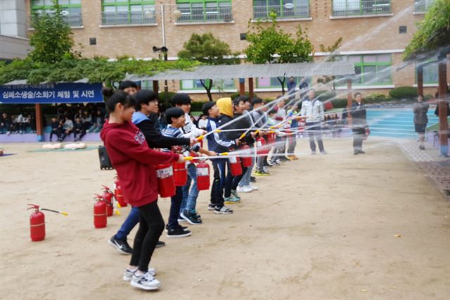 지난달 26일 인천 만석초등학교에서 열린 두산인프라코어의 안전문화 사회공헌활동에서 학생들이 소화기 사용법을 체험하고 있다. 두산인프라코어 제공