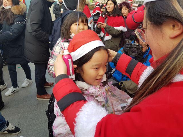 24일 오후 서울 광화문광장에서 한 청년 산타가 9차 촛불집회에 참가한 어린이에게 선물을 나눠주고 산타 모자를 씌어주고 있다.