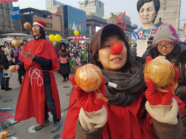 예술가 모임인 ‘주류아닌예술가들’ 회원 5명이 24일 오후 서울 광화문광장에서 산타 복장을 하고 ‘양파-까도까도 끝이 없다’라는 주제로 시민참여 행사를 진행하고 있다. 회원들은 “양파처럼 까도 까도 끝없이 나오는 박근혜 정권의 비리에 영감을 받아 시민들과 양파까기 행사를 마련했다”고 말했다.