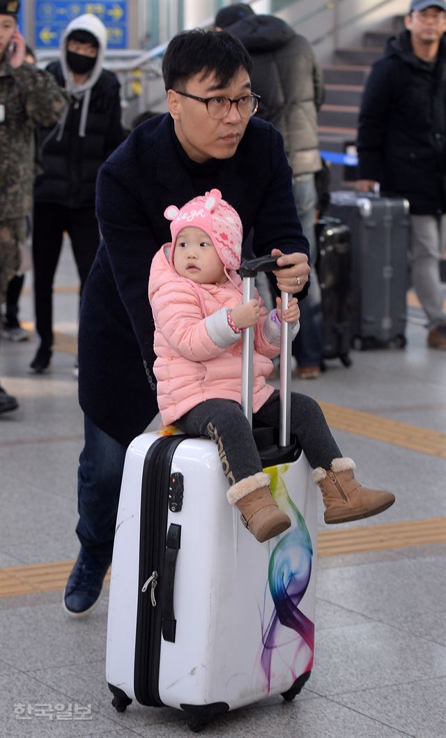 아빠가 밀어주는 캐리어를 타고 이동하는 한 아이.