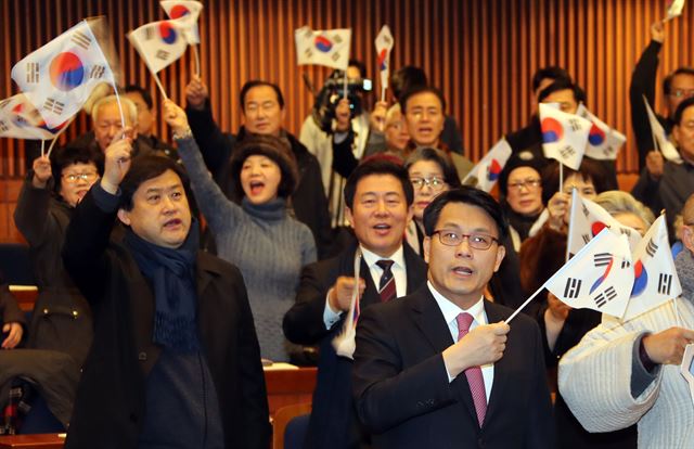 새누리당에서 당원권 1년 정지 처분을 받은 윤상현(맨 앞) 의원이 9일 국회 헌정기념관에서 자기가 주최한 ‘태극기 민심의 본질은 무엇인가’ 토론회에서 참석자들과 함께 태극기를 흔들며 애국가를 부르고 있다. 연합뉴스