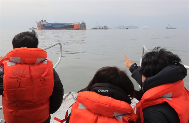 세월호 미수습자 가족들이 26일 오전 전남 진도군 세월호 사고 수습 인근에서 반잠수선에 실려 온전히 모습을 드러낸 세월호를 바라보고 있다. 2∼4일로 예상되는 배수를 거치면 세월호는 반잠수선과 고박을 단단히 하고 목포 신항을 향해 '마지막 항해'에 나선다. 연합뉴스