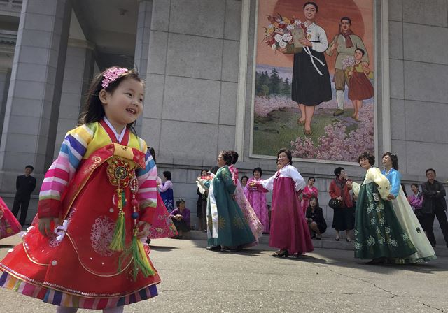 북한 인민군 창건 85주년을 맞은 25일 평양에서 색동저고리 한복을 입은 한 소녀가 경축무도회에 참여해 춤울 추고 있는 주민들을 바라보고 있다. 북한은 이날 강원도 원산 일대에서 역대 최대 규모의 화력훈련을 진행하고 있는 것으로 알려졌다. AP 연합뉴스