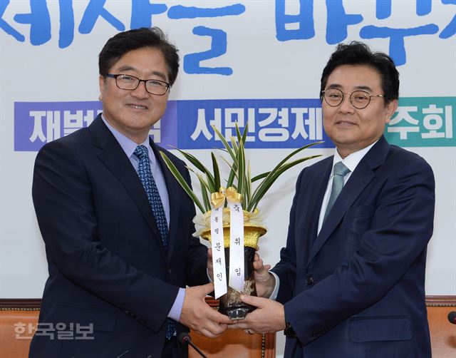 더불어민주당 우원식 신임 원내대표가 17일 오전 국회 원내대표실에서 취임 축하차 방문한 전병헌 청와대 정무수석으로부터 문재인 대통령 명의의 축하 난을 받고 있다. 오대근기자 inliner@hankookilbo.com