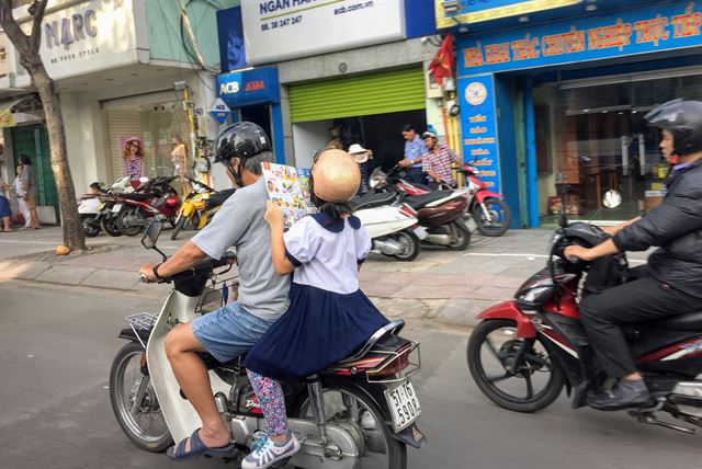 베트남 호찌민 도심에서 한 학생이 오토바이 뒷좌석에 앉아 책을 보고 있다.