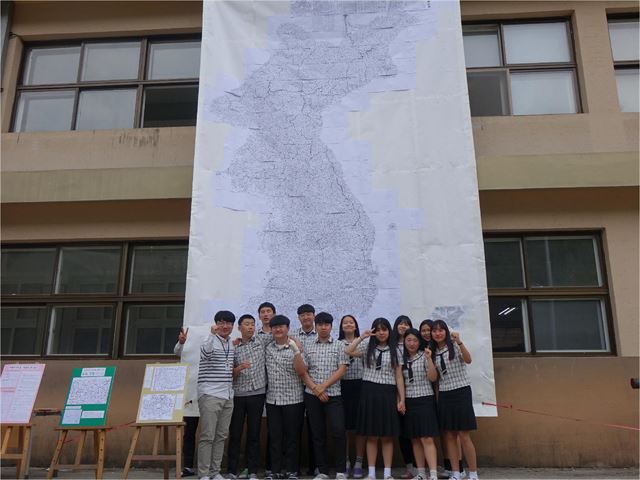 충주 충원고 지리답사동아리 ‘너나들이’ 학생들이 실제 크기로 제작한 대동여지도를 학교 건물 앞에 내걸고 기념촬영을 했다. 맨 왼쪽은 한국지리를 가르치는 유성희 교사. 충원고 제공