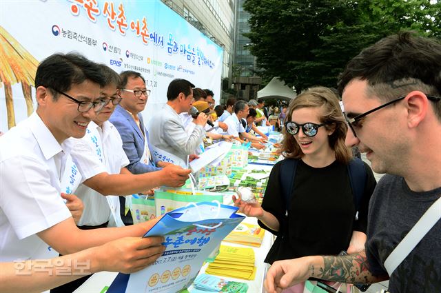 농협중앙회,농식품부 등 관계자들이 20일 오전 서울 광화문 동화면세점 앞에서 여름 휴가 농촌ㆍ산촌ㆍ어촌에서 보내기 캠페인을 진행, 시민들에게 홍보 책자와 지도, 부채 등을 전달하고 있다.고영권기자youngkoh@hankookilbo.com