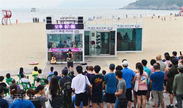 22일 오후 부산 해운대해수욕장 ‘해운대 해변 라디오ㆍ북 카페’에서 ‘해변 라디오’가 열려 많은 관광객들이 마술공연을 관람하고 있다. 이 프로그램은 목, 금, 토, 일 오후 7시부터 1시간 동안 진행된다.