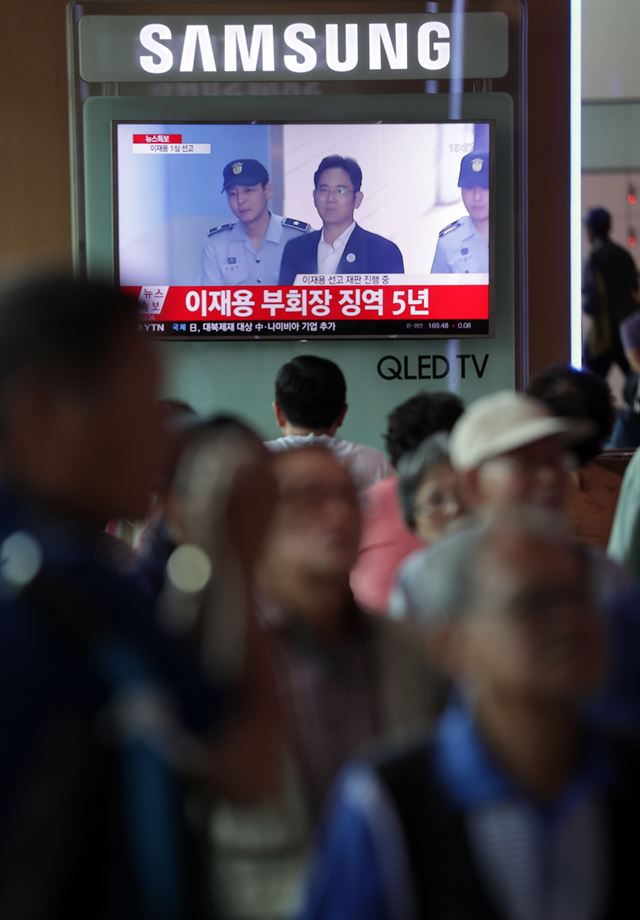 지난 25일 오후 서울역에서 시민들이 대합실에 설치된 삼성전자 TV로 이재용 삼성전자 부회장의 선고 관련 뉴스를 지켜보고 있다. 연합뉴스