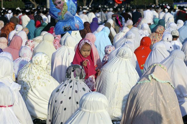 이슬람권 명절인 '이드 알 아드하(희생제)' 를 맞은 1일(현지시간) 인도네시아 발리에서 아침 기도를 하고 있는 여성 무슬림들 사이에 한 어린이가 '겨울왕국'의 캐릭터 엘사 풍선을 들고 서 있다. AP 연합뉴스