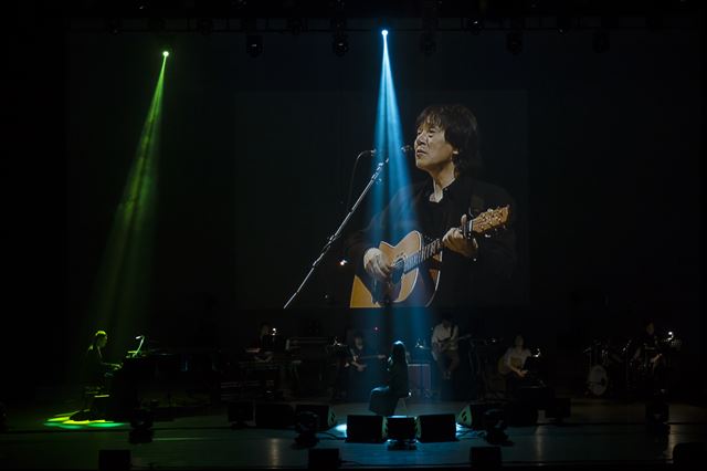 가수 장필순이 16일 서울 서초동 한전아트센터에서 열린 조동진 추모 공연 ‘우리 같이 있을 동안에’에서 고 조동진의 영상을 보며 고인이 남긴 ‘제비꽃’을 부르고 있다. 푸른곰팡이 제공