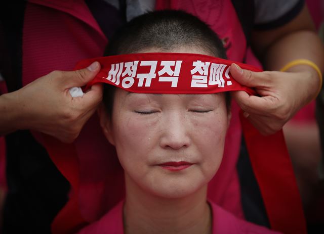 19일 오전 정부서울청사 앞에서 열린 전국학교비정규직노동조합원들의 근속수당 인상 및 교육부장관·교육감 직접 교섭 촉구 집단삭발식에서 한 조합원이 삭발을 마친 뒤 머리띠를 두르고 있다. 연합뉴스