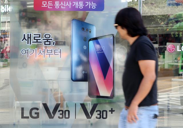 각 이동통신업체가 LG전자의 스마트폰 V30를 출시한 21일 서울 동대문구 한 휴대폰 판매점에서 시민이 V30 광고 앞을 지나고 있다. 연합뉴스