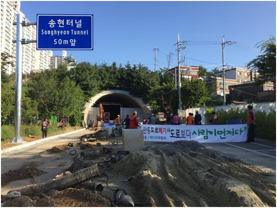 인천 중구 신흥동 삼익아파트와 동구 동국제강간 도로 건설 사업 중단을 요구하고 있는 ‘중ㆍ동구 관통 도로 전면폐기 대책위원회’ 관계자들이 지난달 13일 도로 1ㆍ2구간을 연결하는 송현터널 입구에서 ‘도로보다 사람이 먼저다’라고 적힌 현수막을 펼치고 있다. 중ㆍ동구 관통 도로 전면폐기 대책위원회 제공