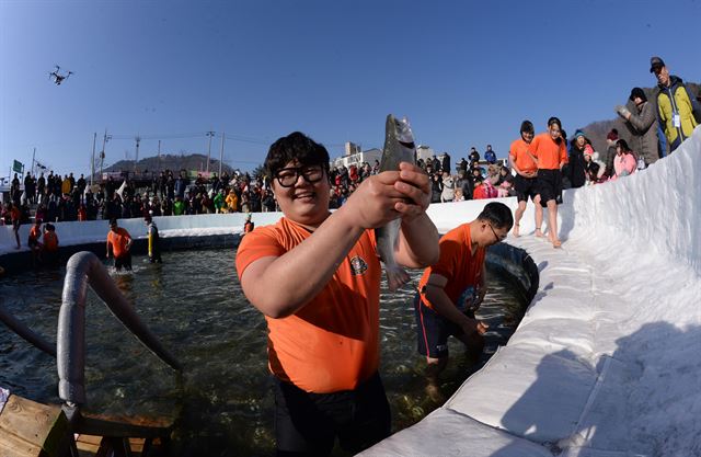 화천 산천어축제장을 찾은 관광객이 맨손잡기 체험장에서 산천어를 잡아 들어올린 뒤 함박웃음을 짓고 있다. 화천군 제공