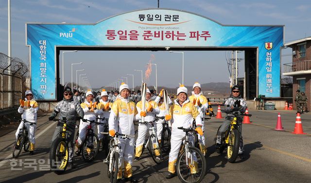 [저작권 한국일보] 가수 김창완(오른쪽에서 세번째)씨와 목함지뢰 사건 당시 수색대를 지휘한 정교성 상사가 평창동계올림픽 성화봉송 민간인출입통제선(민통선) 구간 첫째 날인 19일 경기 파주시 통일대교에서 토치키스(성화 교대)를 하고 있다. 파주=김주영 기자