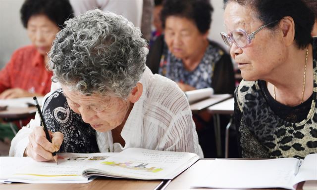 경로당에 개설한 한글학교에서 받아쓰기 수업 중인 할머니를 동료 할머니가 지켜보고 있다. 논산시 제공