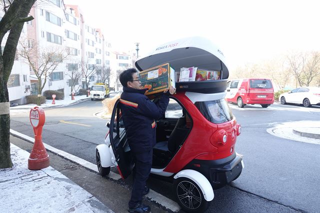 우정사업본부는 앞으로 3년 안에 집배원들이 현장에서 우편물이나 택배를 분리하고 정리하고 배포하는 과정에서 쓰는 초소형전기차 1만대를 보급하겠다고 밝혔다. 사진은 한 집배원이 지붕 위 짐 싣는 공간에서 우편물을 꺼내고 있다. 우정사업본부 제공