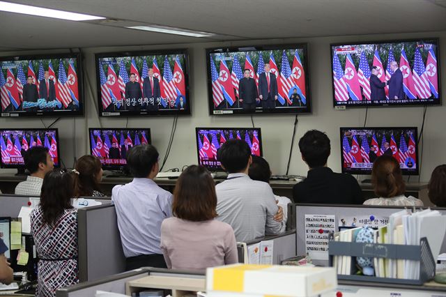 12일 오전 서울 세종로 정부서울청사에서 공무원들이 김정은 북한 국무위원장과 도널드 트럼프 미국 대통령이 북미 정상회담에서 악수하는 모습을 지켜보고 있다. 연합뉴스