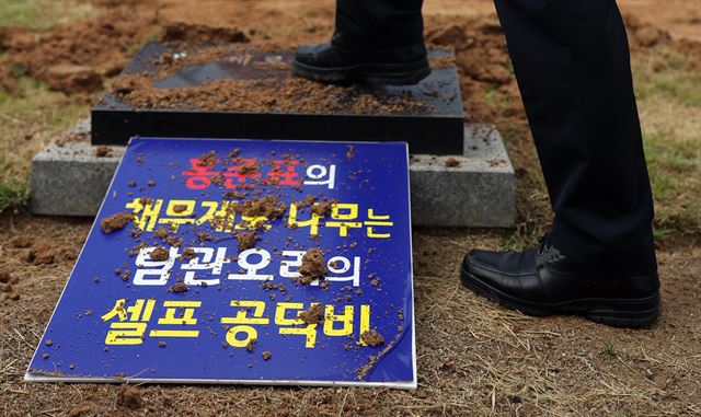 사회단체 관계자가 경남도청 앞에서 홍준표 자유한국당 전 대표가 경남도지사 재직 시절 '경남도 채무 제로'를 기념해 심었던 기념식수 앞에 설치된 표지석을 밟고 있다. 연합뉴스