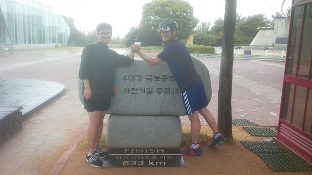 신한은행에서 일하는 김백년(오른쪽)씨가 2015년 8월 중학생 아들 형일군과 자전거 국토종주를 마치고 종착지인 부산 사하구 낙동강 하구둑 인증센터에서 손을 맞잡고 있다. 김백년씨 제공