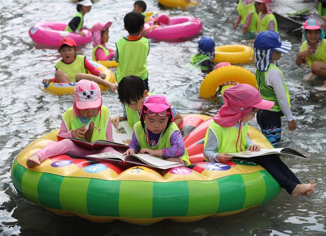 24일 서울 송파구 성내천에서 어린이들이 물놀이를 하며 독서하는 모습을 연출하고 있다. 송파구는 성내천 물놀이장에 도서를 비치하고, 파라솔과 테이블 등 독서 공간을 제공하는 '여름행복문고'를 오는 이달 말까지 운영한다. 연합뉴스