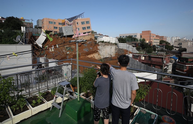 7일 오전, 주민들이 전날 발생한 공사장 옹벽 붕괴 사고의 여파로 금방이라도 무너질 듯 위태로운 상도유치원 건물을 바라보고 있다. 연합뉴스