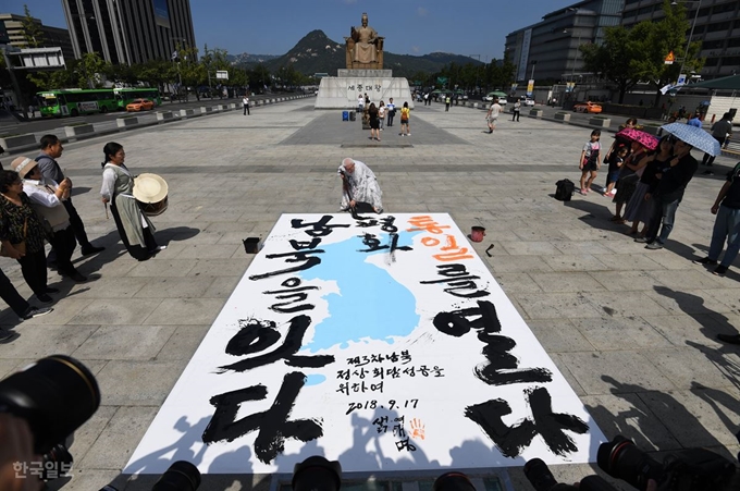 여태명 원광대학교 미술대학 교수가 제3차 평양 남북정상회담을 하루 앞둔 17일 오후 서울 광화문광장 세종대왕상 앞에서 '남북을 잇다, 통일을 열다' 대형 붓글씨를 쓰고 있다. 서재훈 기자