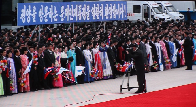 '2018남북정상회담평양'의 첫 날인 18일 오전 평양 순안공항에서 북측 환영인파가 문재인 대통령의 도착을 기다리는 장면이 이날 서울 중구 DDP 메인프레스센터에 중계되고 있다. '평양을 방문하는 문재인 대통령을 열렬히 환영합니다!' 환영 문구가 보인다. 연합뉴스